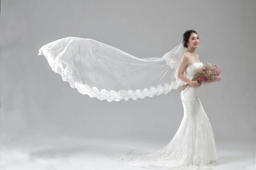 ベールを後ろになびかせて笑顔でこちらをみているウェディングドレス姿の新婦