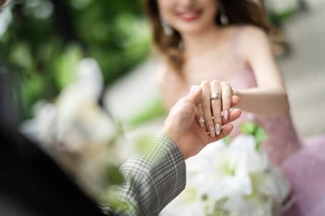 手前から新郎が体を伸ばし、奥側からその手を取るピンクのドレス姿の新婦