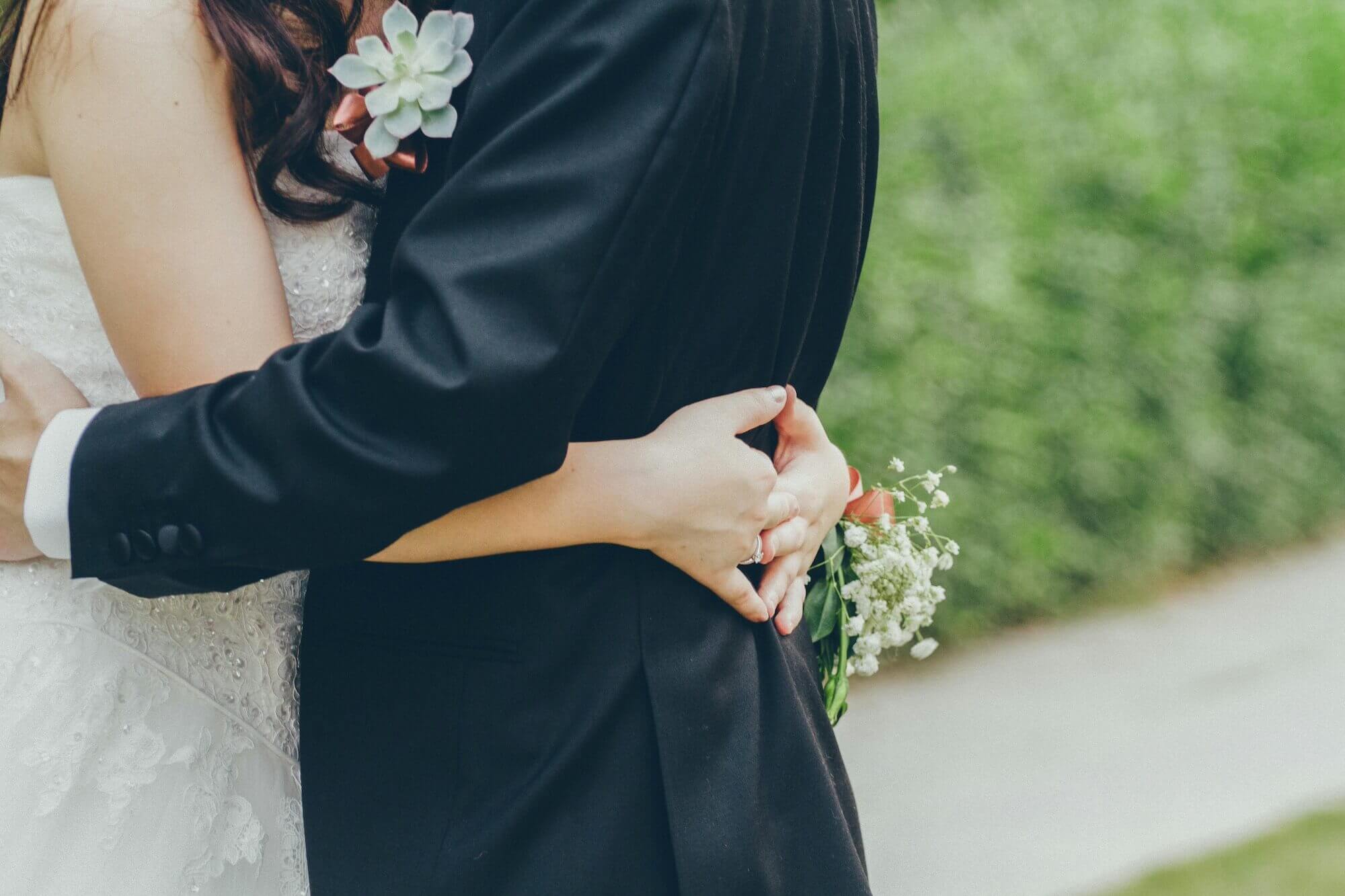 緑の森を背景に、タキシード姿の新郎とウェディングドレス姿の新婦が抱き合っている