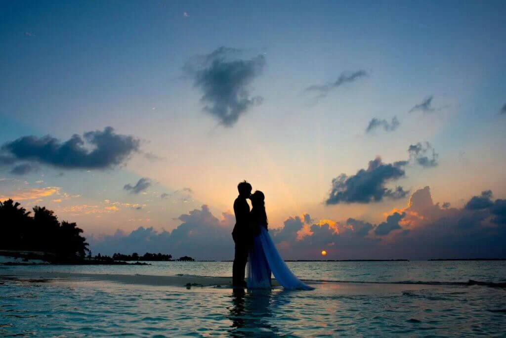 夕日が落ちた薄暗い中、海の中に立って、キスをしている新郎と新婦。