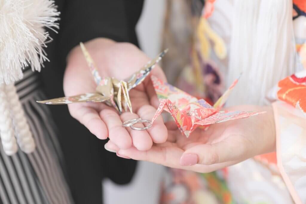 和装姿の新郎新婦の手のひらに乗せられた一対の和柄の折鶴