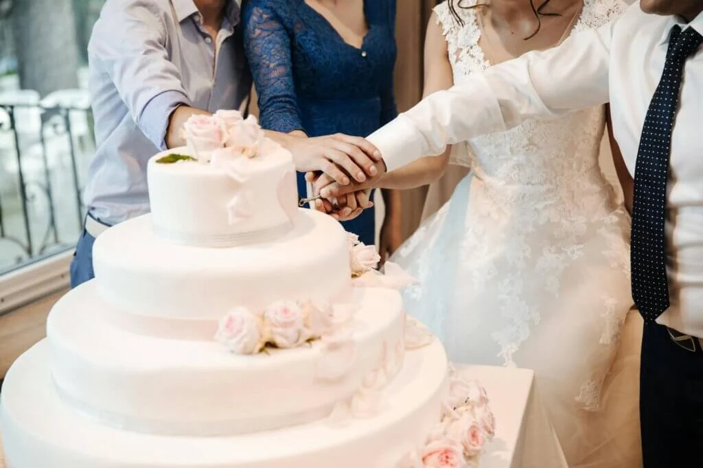 薄いピンクの4段の丸いウェディングケーキに、入刀している新郎新婦とゲストカップル
