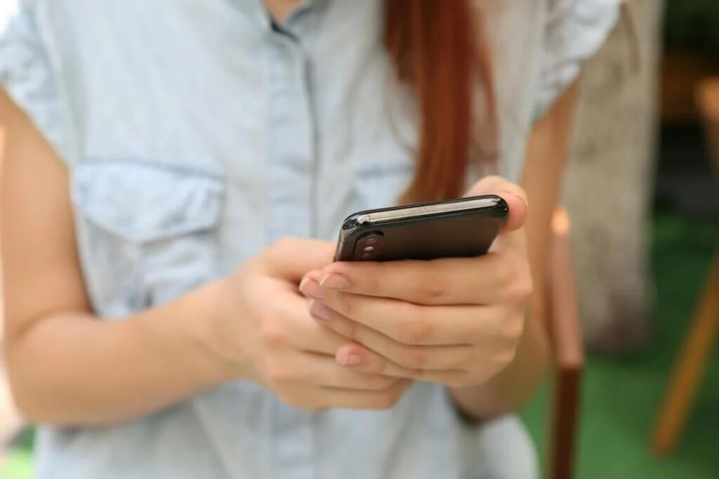 女性が両手でスマートフォンを持ち、操作している。