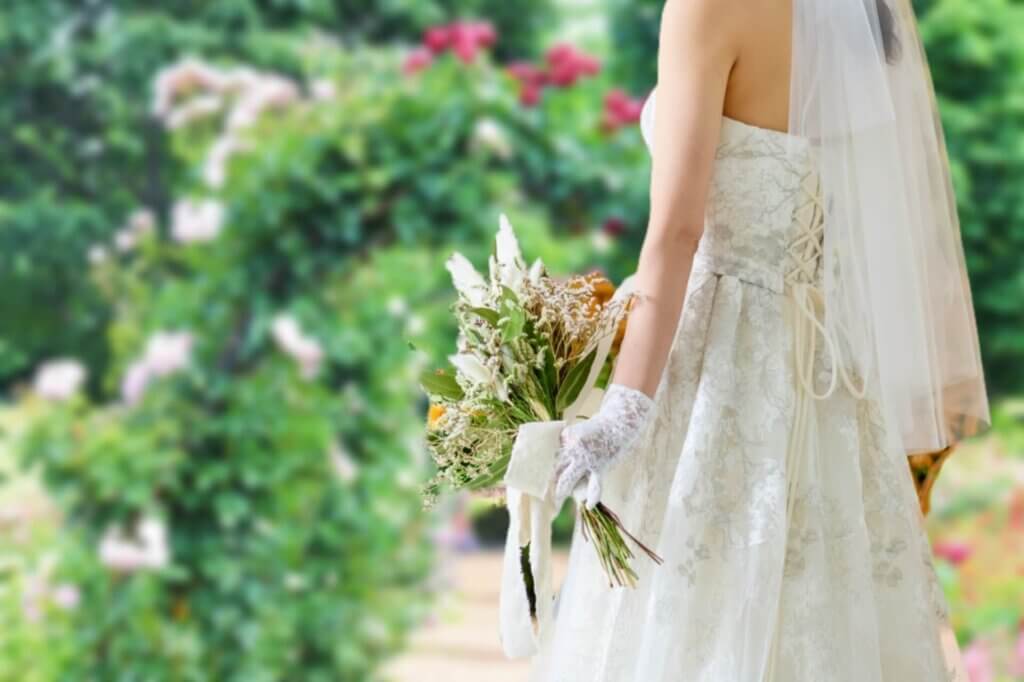 手に白いブーケを持ち、ガーデンの前でたたずんでいる新婦
