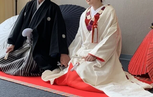 紋付袴と白い和装姿の新郎新婦が座している