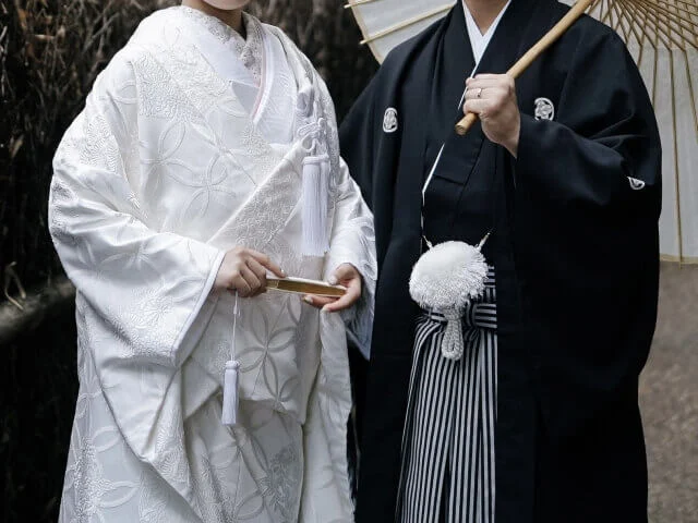 紋付袴と白無垢姿の新郎新婦。新郎が肩に番傘をもられかけさせている。