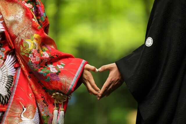 紋付袴と色打掛姿の新郎新婦がお互いの手をあわせてハート型を形作っている