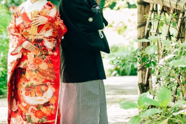 紋付袴と色打ち掛け姿の新郎新婦が和の庭園で佇んでいる