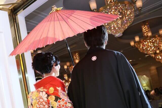 赤い番傘をさしながら、紋付袴と色打ち掛け姿で披露宴会場に入場する新郎新婦