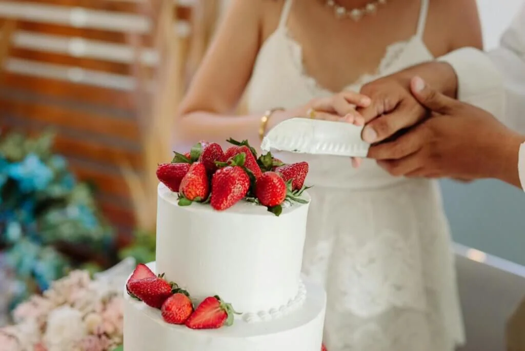 たくさんのイチゴが盛り付けられた純白の2段のウェディングケーキに新郎新婦がナイフを入れようとしているところ。