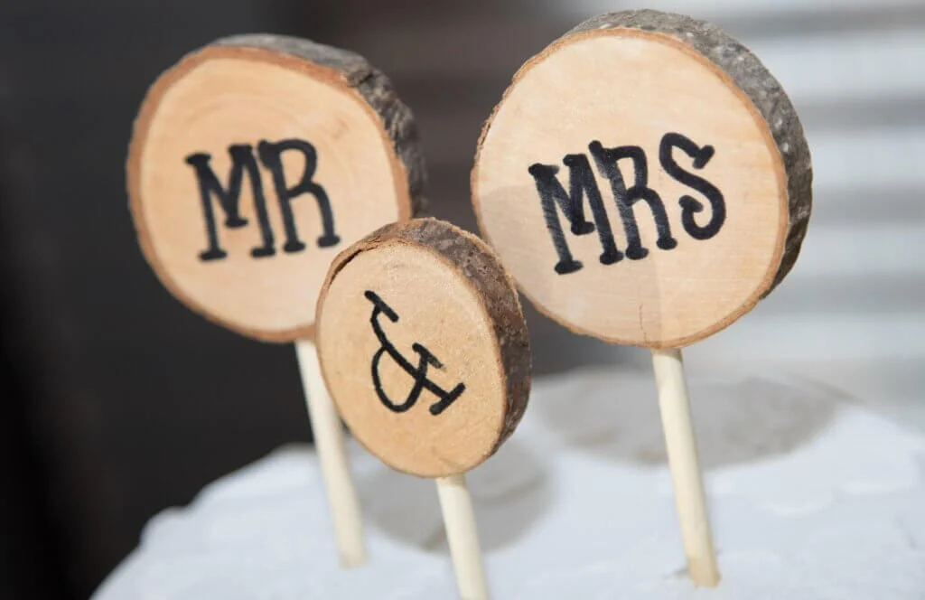 3つの切り株にMR、MRS、＆が書かれており、そのオブジェがウェディングケーキの上に刺さっている