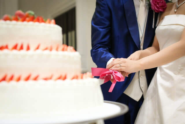 大きな散弾のウェディングケーキにたくさんのケーキが飾られている。そこに新郎新婦がケーキ入刀を行っている。