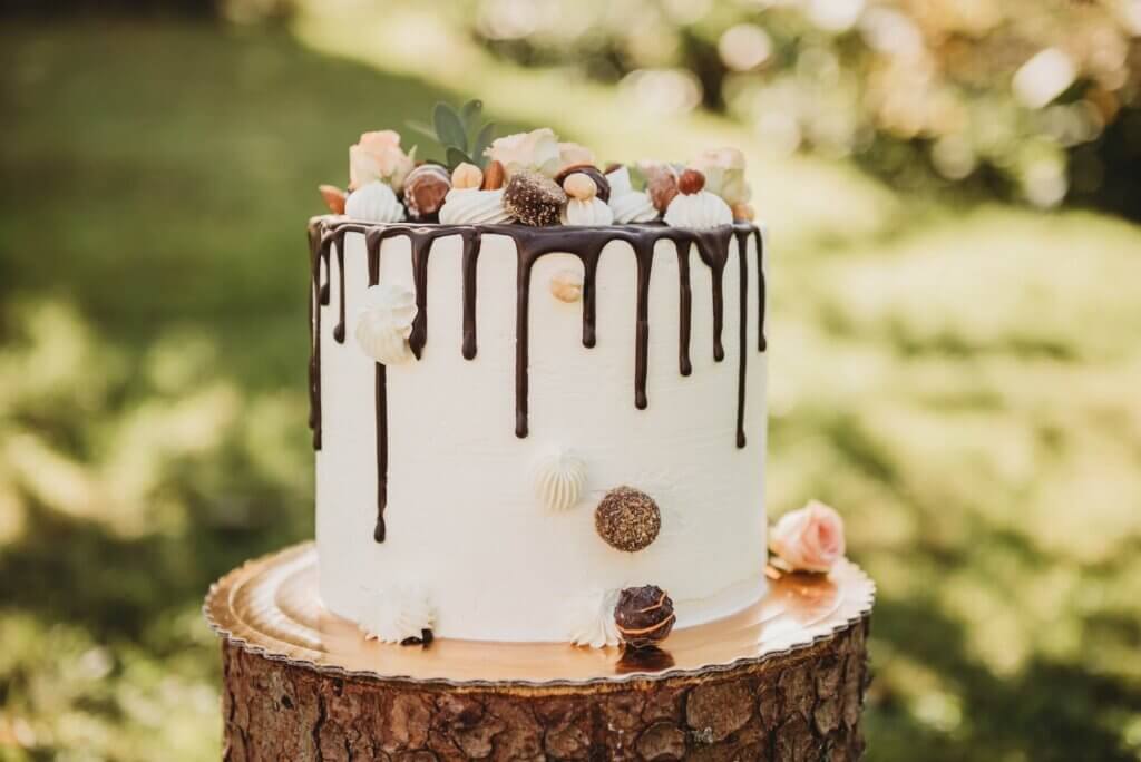 切り株の上に置かれたチョコレートドリップが滴っている白いウエディングケーキ。