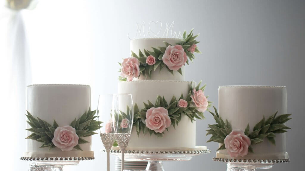 真ん中に、円柱で2段のピンクのバラがデコレーションされたウェディングケーキが配置され、両脇に同じデコレーションの1段型のケーキが配置されている