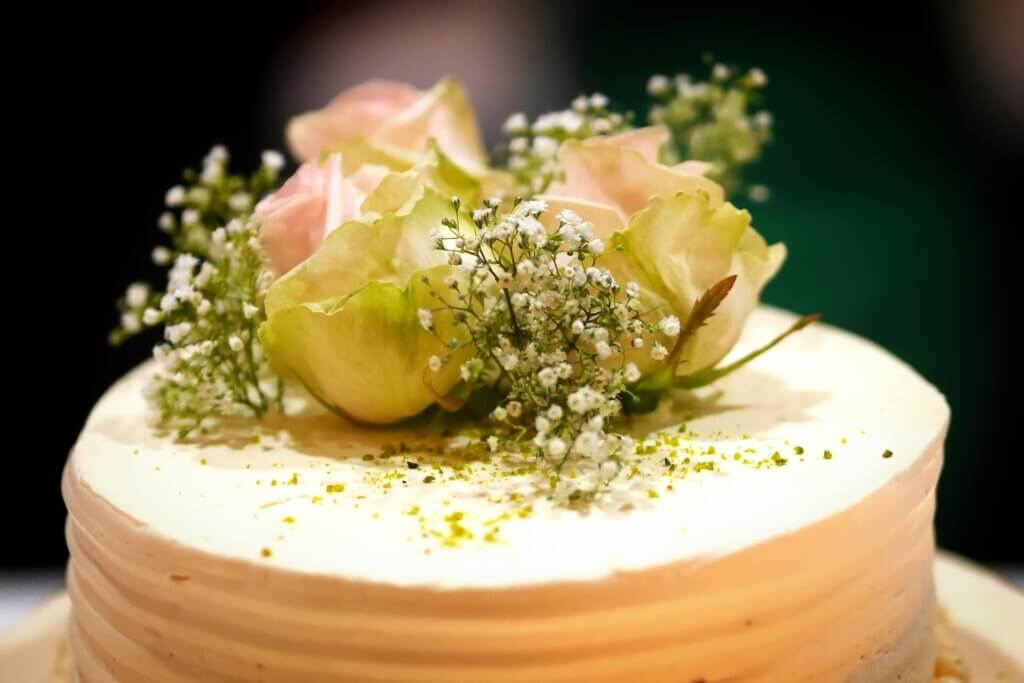 白ケーキの上に霞草とピンクとグリーンの葉が混ざったバラが配置されている