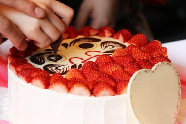 イチゴとチョコレートでダルマのデコレーションがされている純白のケーキ