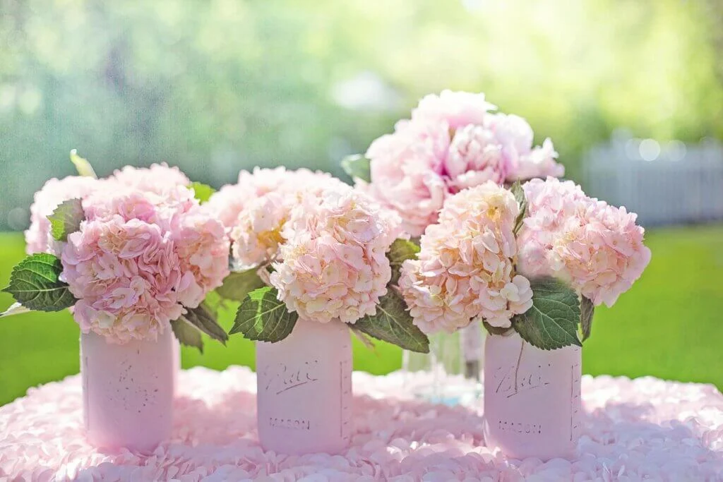 ピンクの花びらで敷き詰められたテーブルの上にその花が4つの花瓶にいけられている