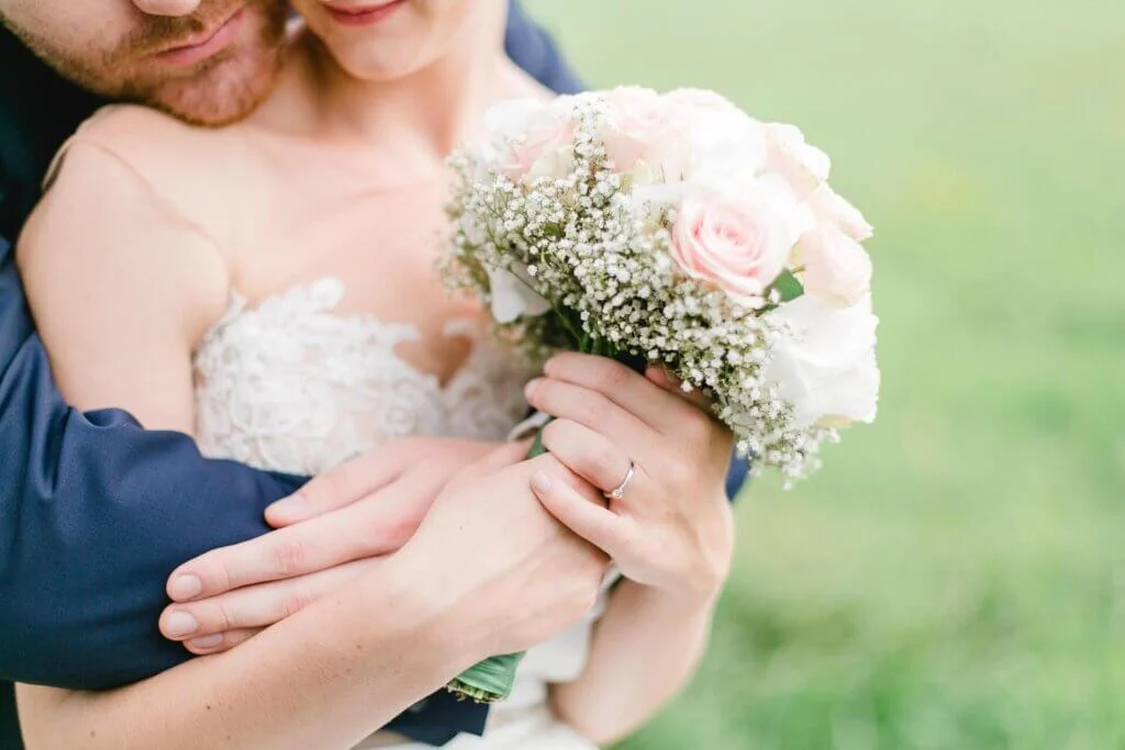 ピンクのバラのブーケを持つ新婦をバックハグする新郎