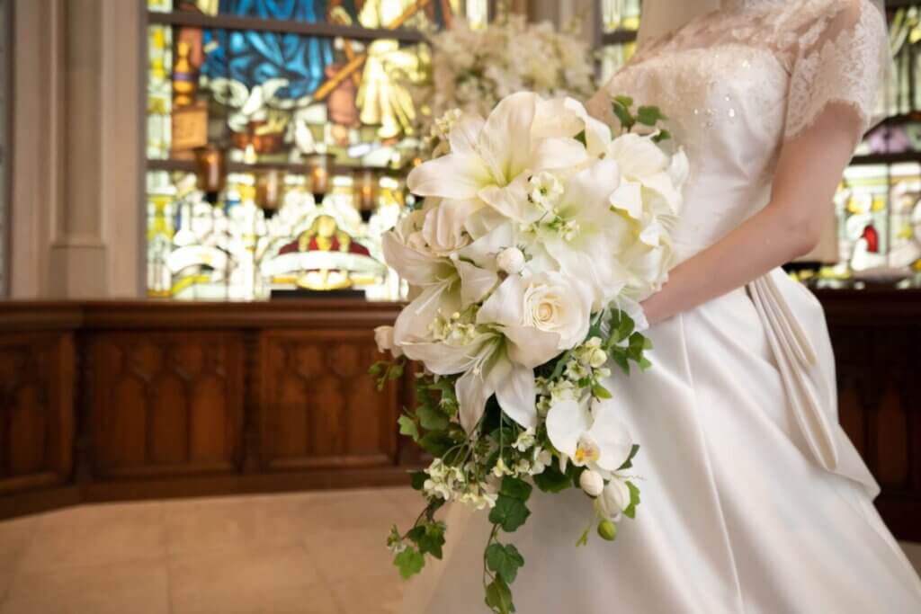 チャペルのステンドグラスの前で、大きな白い花のブーケを持つ新婦