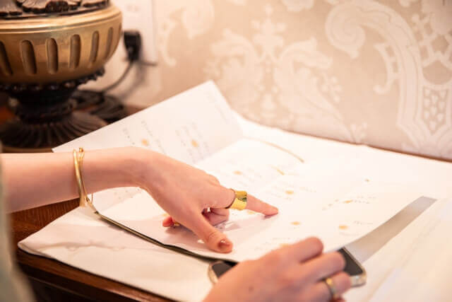 披露宴会場の受付で、紙の席次表を指差しながら自分の座席を確認するゲストの手元。