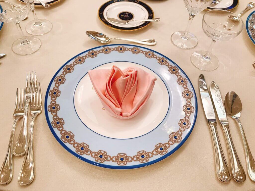 フルコースのナイフセットが置かれた。真ん中に薄いブルーの大きなお皿が置かれ、その上にピンクのバラを片取ったナフキンが配置されている。