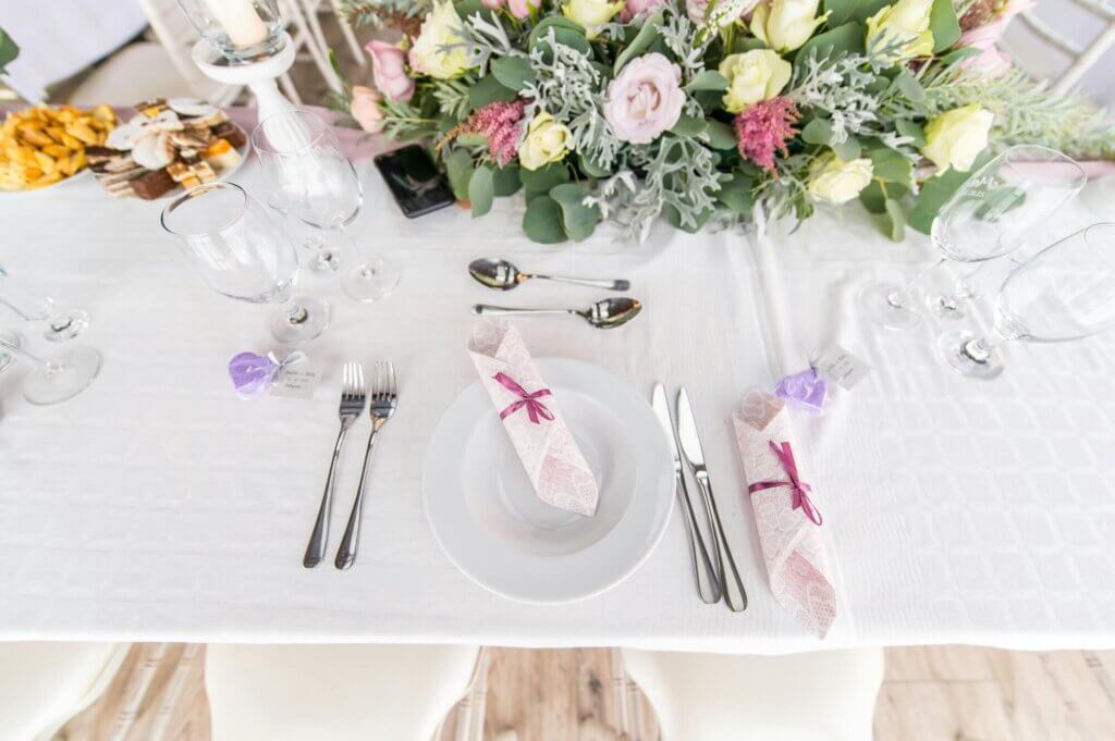 白いテーブルクロスの上にナイフ。フォークセットが配置されており、真ん中に白いお皿のとピンクの筒状に配置されたの付近が置かれている高砂テーブル。