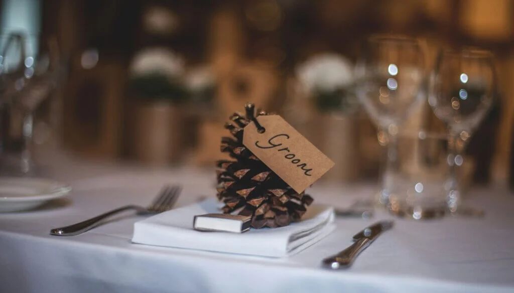 松ぼっくりに「Groom」と書かれたクラフト紙のタグを付けた、秋らしい温かみのある席札。