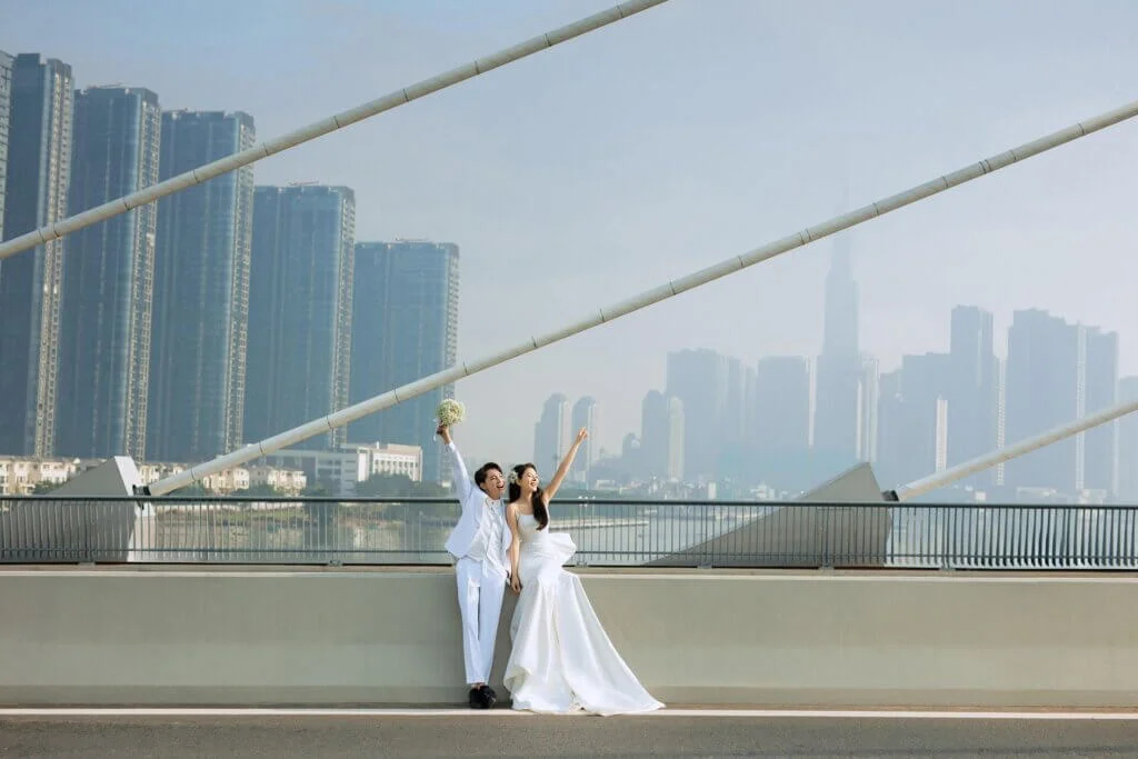 近代的なビル群を背景に、橋の上で喜びを表現するスタイリッシュな新郎新婦