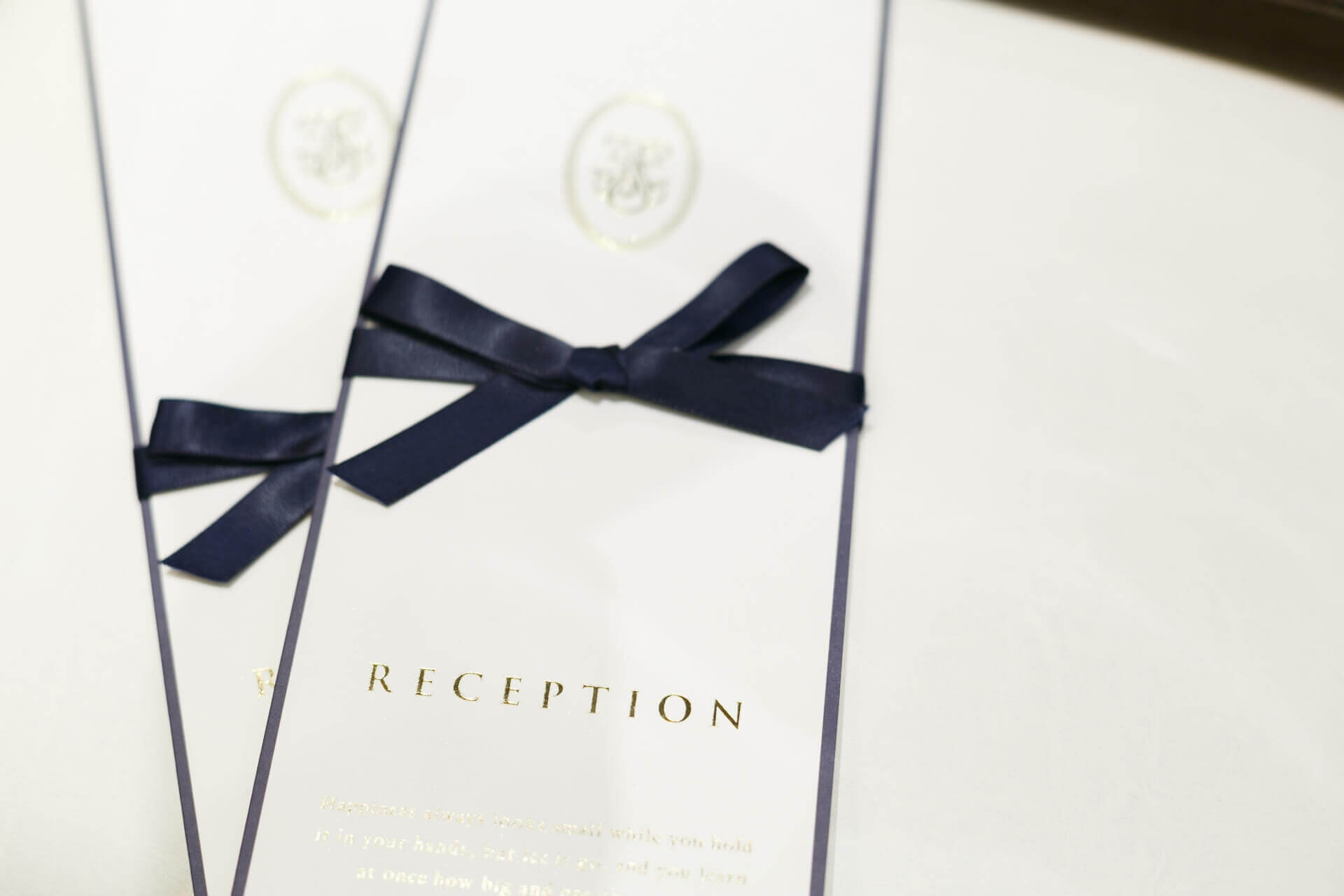 ゴールドの「RECEPTION」という文字が刻まれ、紺色のサテンリボンで装飾された上品な白の席次表(パンフレット)のアップ