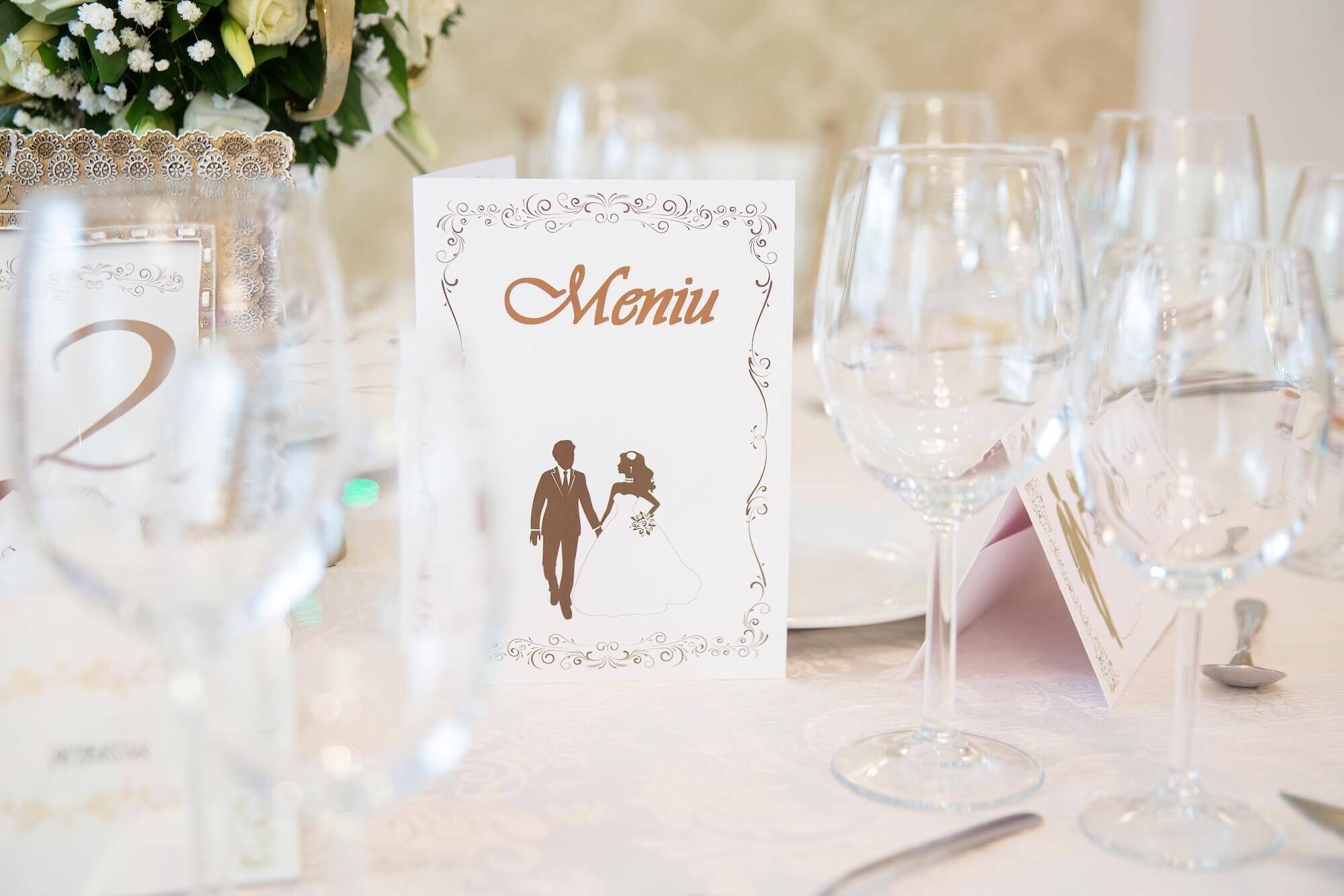 新郎新婦のイラストが描かれた結婚式のメニューカード。ワイングラスが並ぶエレガントなテーブルセット。