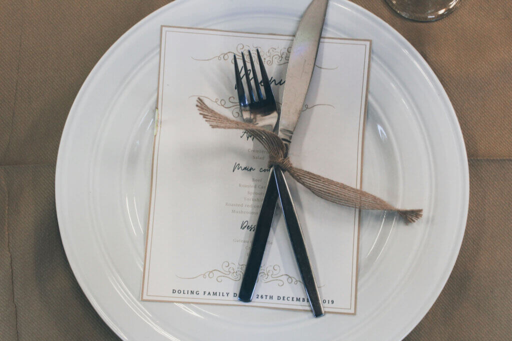 麻紐で結ばれたフォークとナイフが載った結婚式のメニュー表。白い皿の上に置かれたシンプルなデザイン。