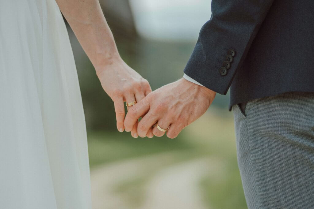 結婚指輪をはめた新郎新婦が、屋外で優しく手を繋いでいる手元のアップ