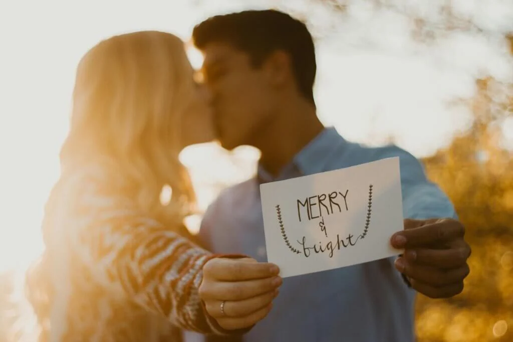 夕陽をバックに「MERRY & BRIGHT」のカードを掲げる、幸せいっぱいの新郎新婦