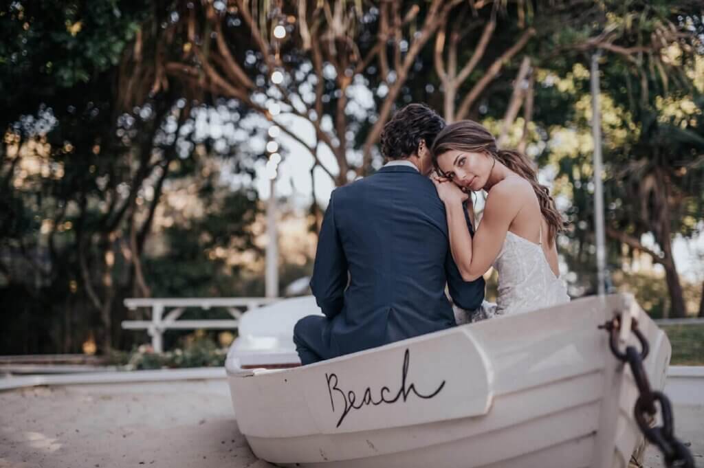 ビーチのボートに座り、新郎の肩に寄り添う新婦。ロマンチックな記念写真。