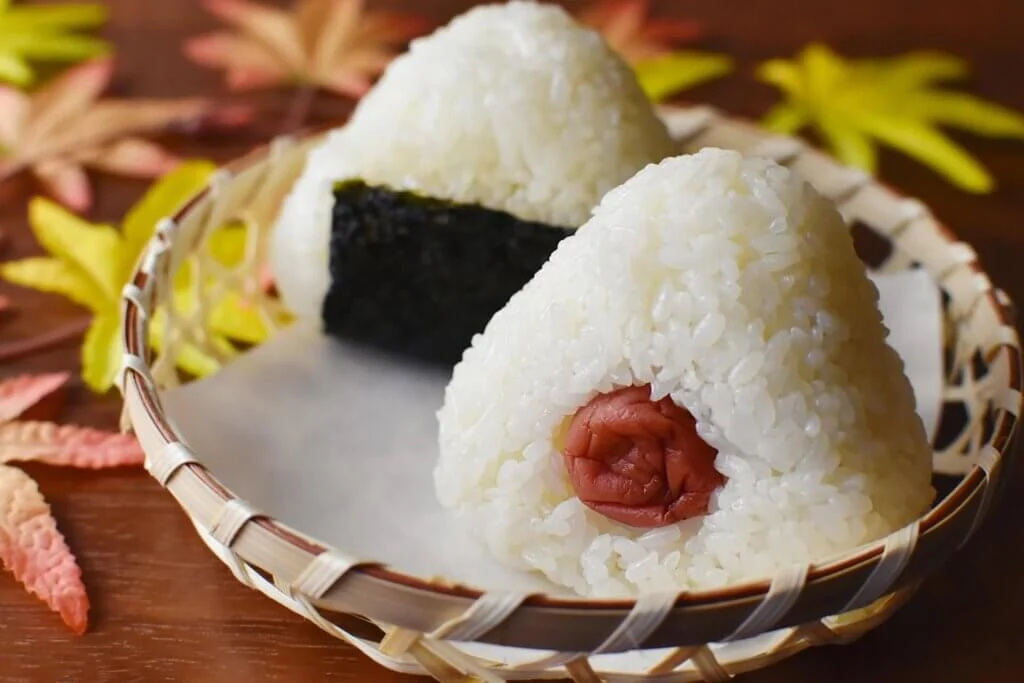 竹かごに盛られた梅干し入りのおにぎりと秋の紅葉を添えた和の食卓