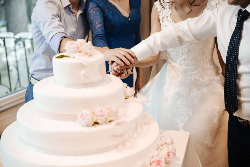 新郎新婦とゲストの手が重なり合い、全員で仲良くナイフを入れてケーキ入刀を行っている様子。
