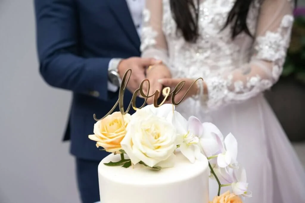 「love」の文字が輝くゴールドのトッパーと、美しいバラや蘭の花で彩られたウェディングケーキ。