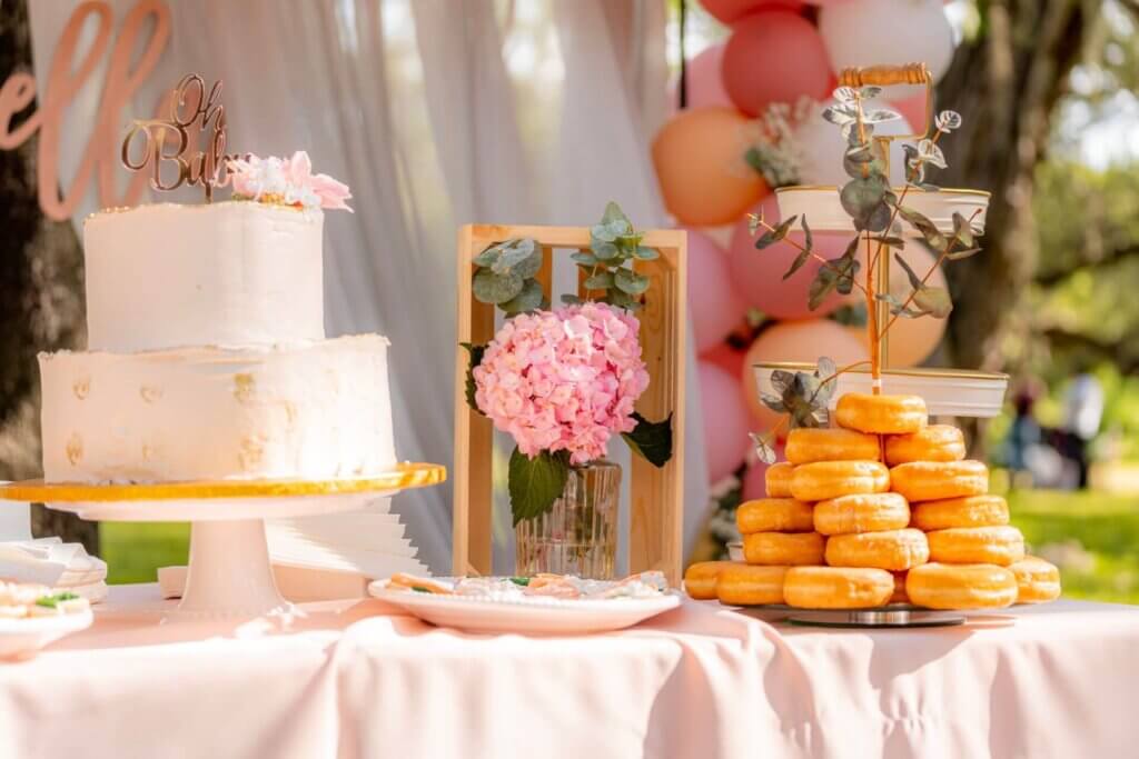 ピンクのバルーンを背景に、ウェディングケーキと美味しそうなドーナツタワーが並ぶ華やかなデザート。
