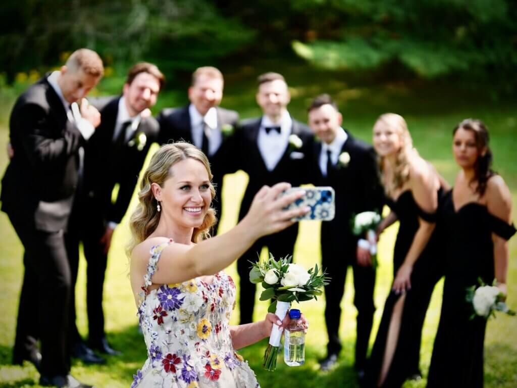 結婚式の屋外で新婦と参列者が楽しそうにスマートフォンで自撮りをする様子