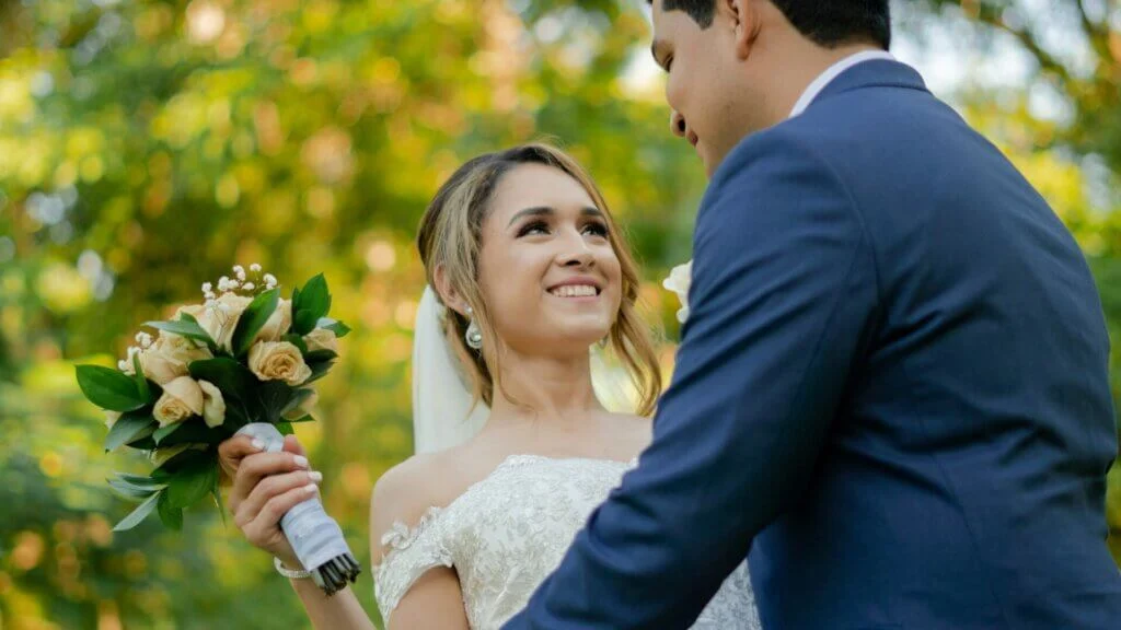 木漏れ日の中で黄色いバラのブーケを持ち新郎を見上げて微笑む新婦