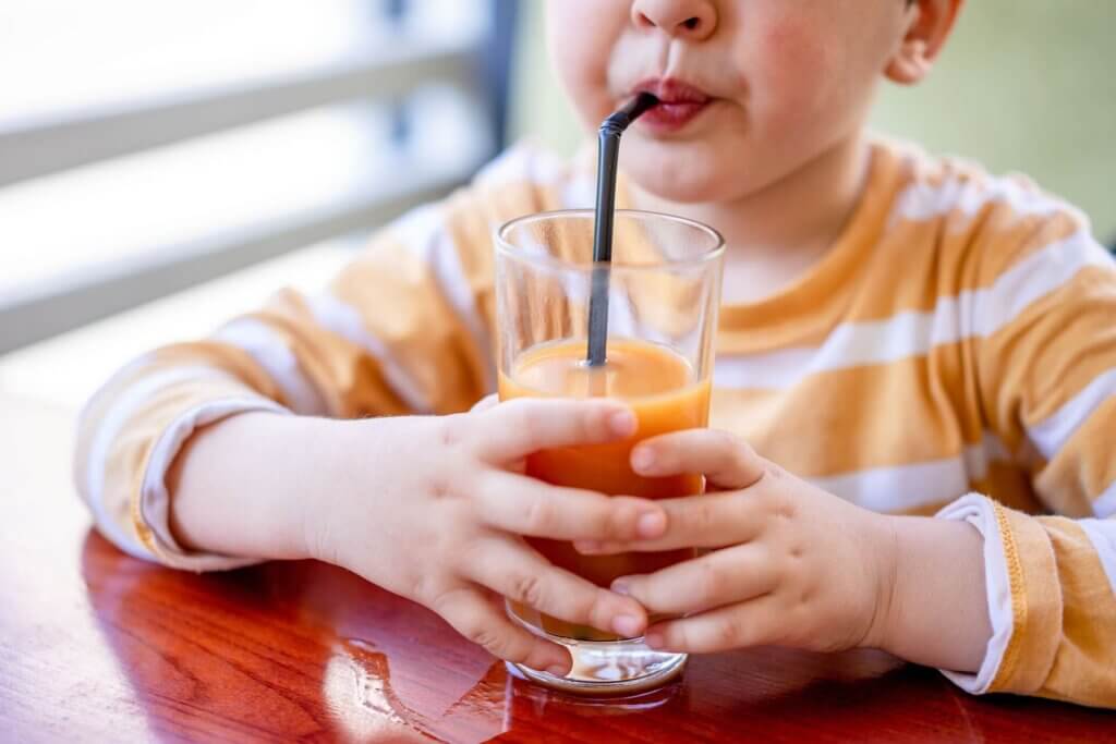 ストローでオレンジジュースを飲む子ども