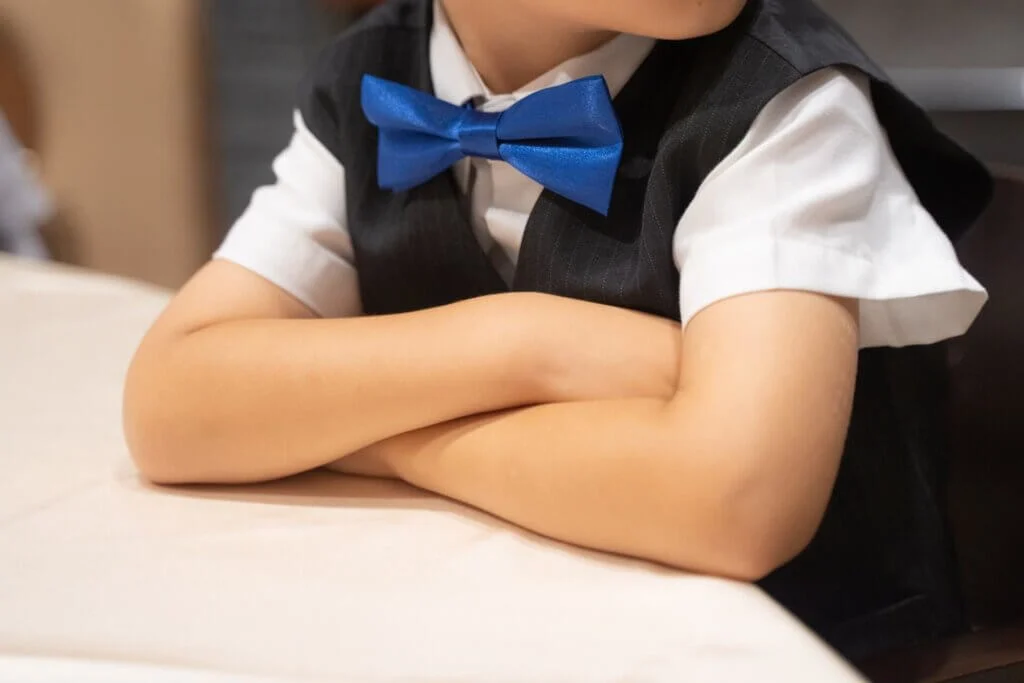 青い蝶ネクタイとベストを着てテーブルにつく男の子