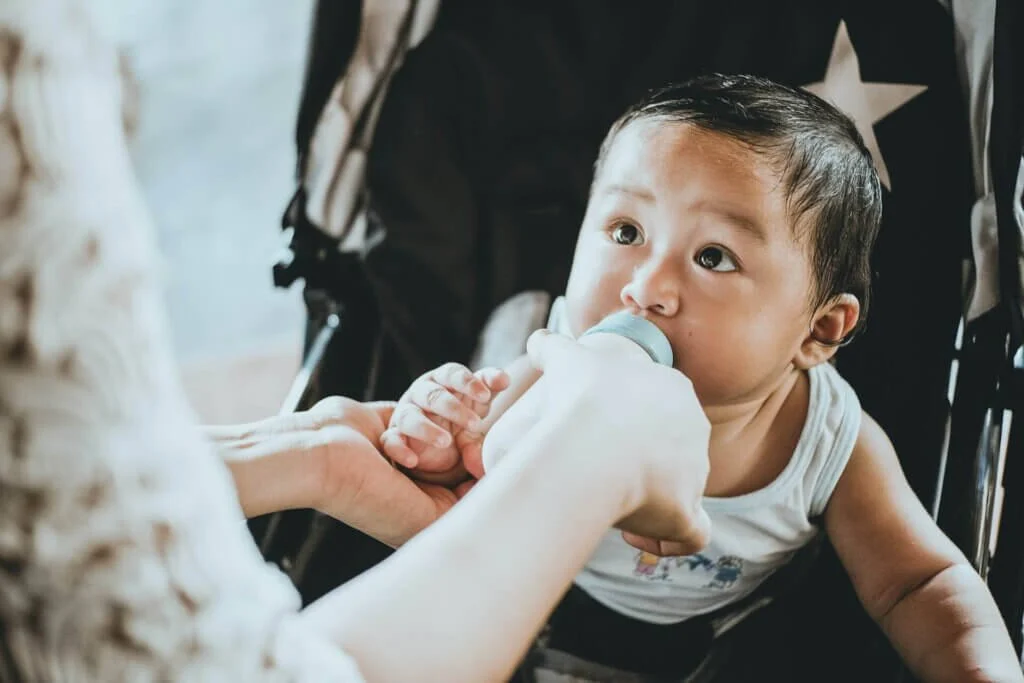 ベビーカーに座って哺乳瓶でミルクを飲む赤ちゃん